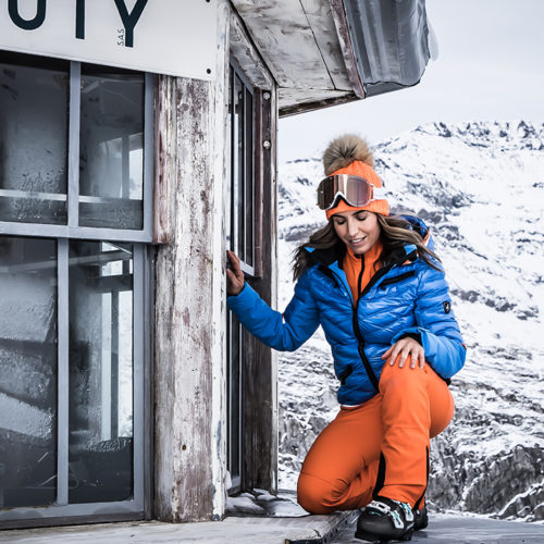 femme en tenue de ski orange et bleue accroupie